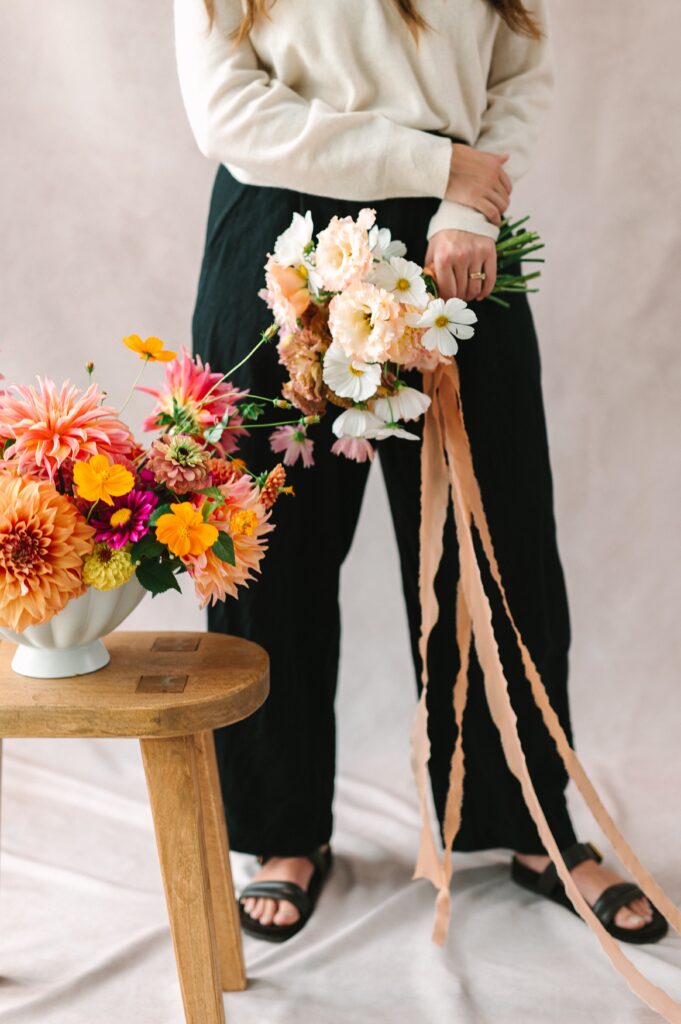 Portrait of Richmond Florist standing next to her floral arrangement and holding a bouquet with a delicate ribbon detail.