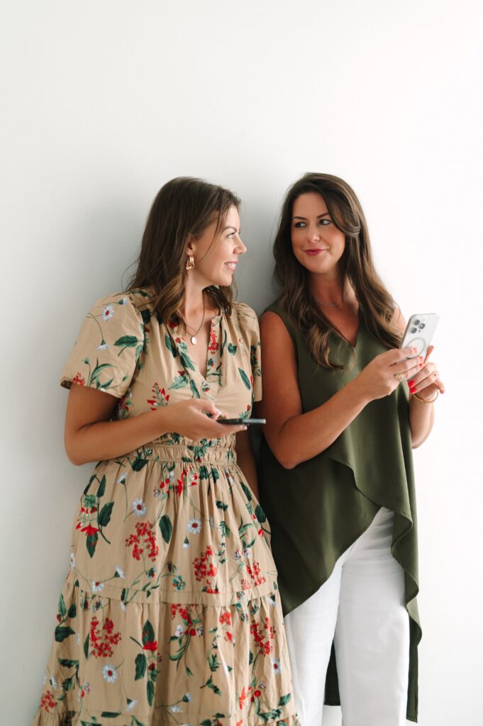 Photograph of two home loan mortgage professionals holding their cell phones and smiling while looking at each other.