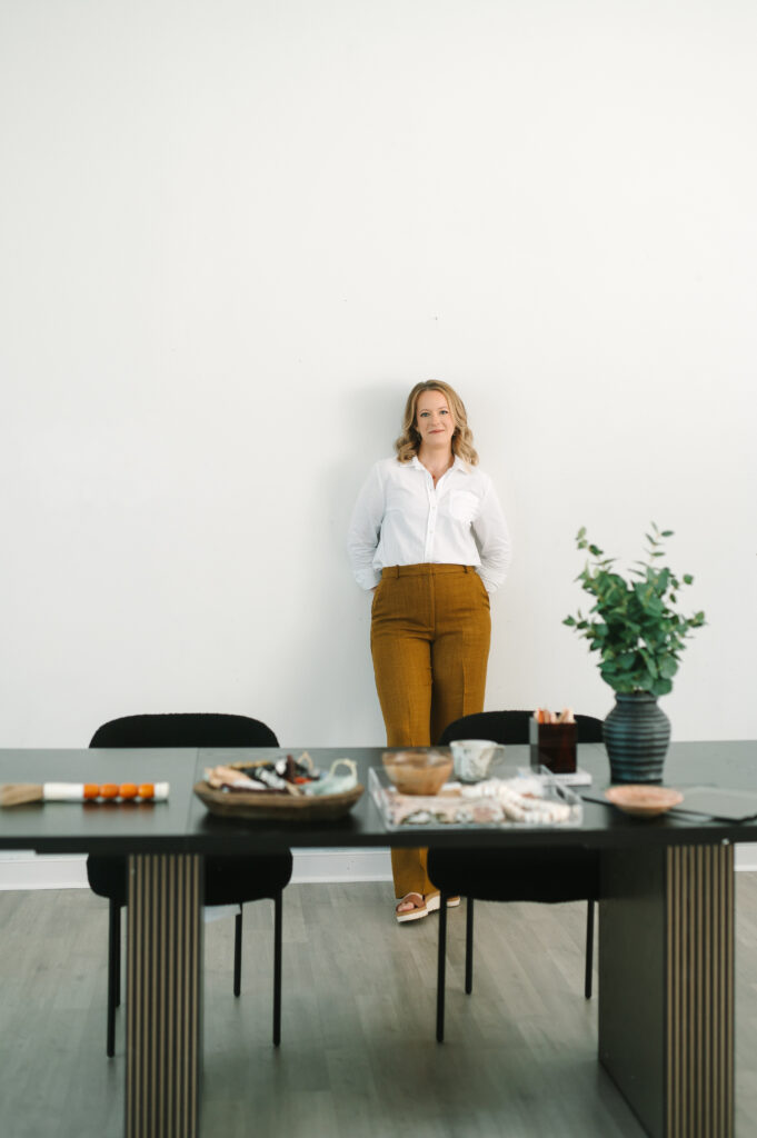 Branding portrait of a woman standing behind a styled desk in a bright Richmond studio.