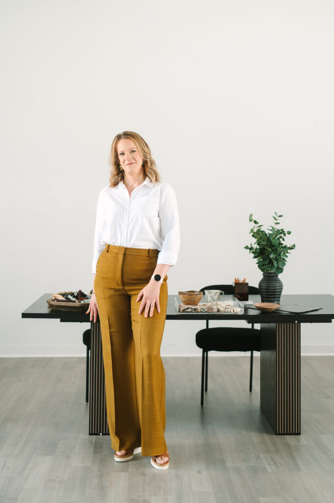 Portrait of a woman standing in a modern Richmond studio with a styled workspace behind her.