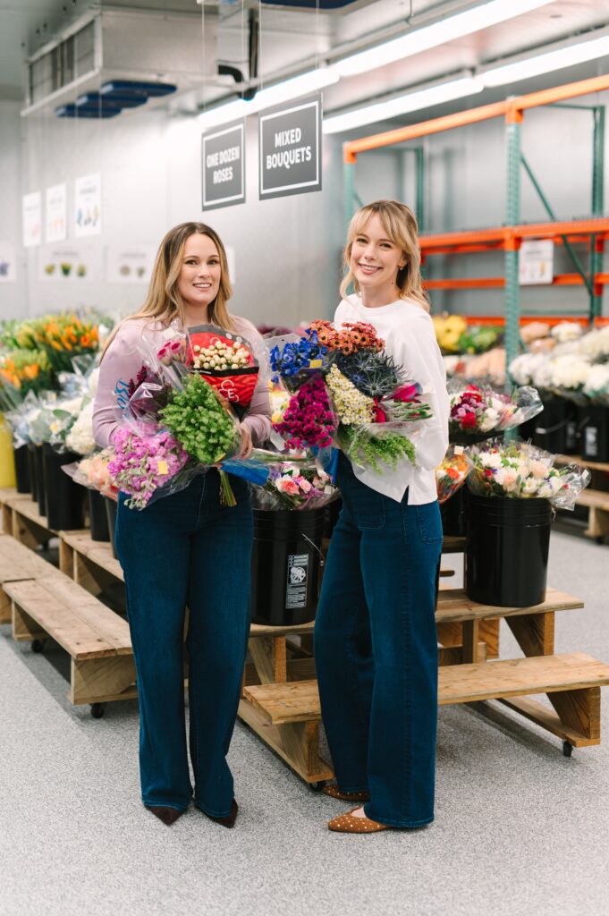 Sister owners of Wholesale Flower Market holding bouquets during branding photography in the floral cooler.