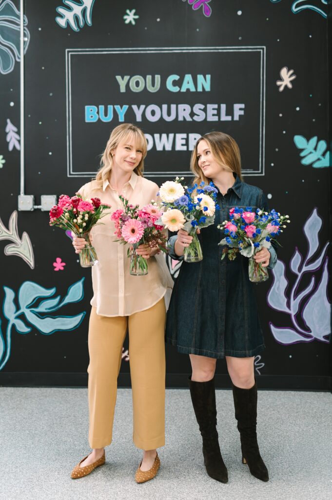 Flower market owners holding colorful arrangements during branding photography in front of a mural.