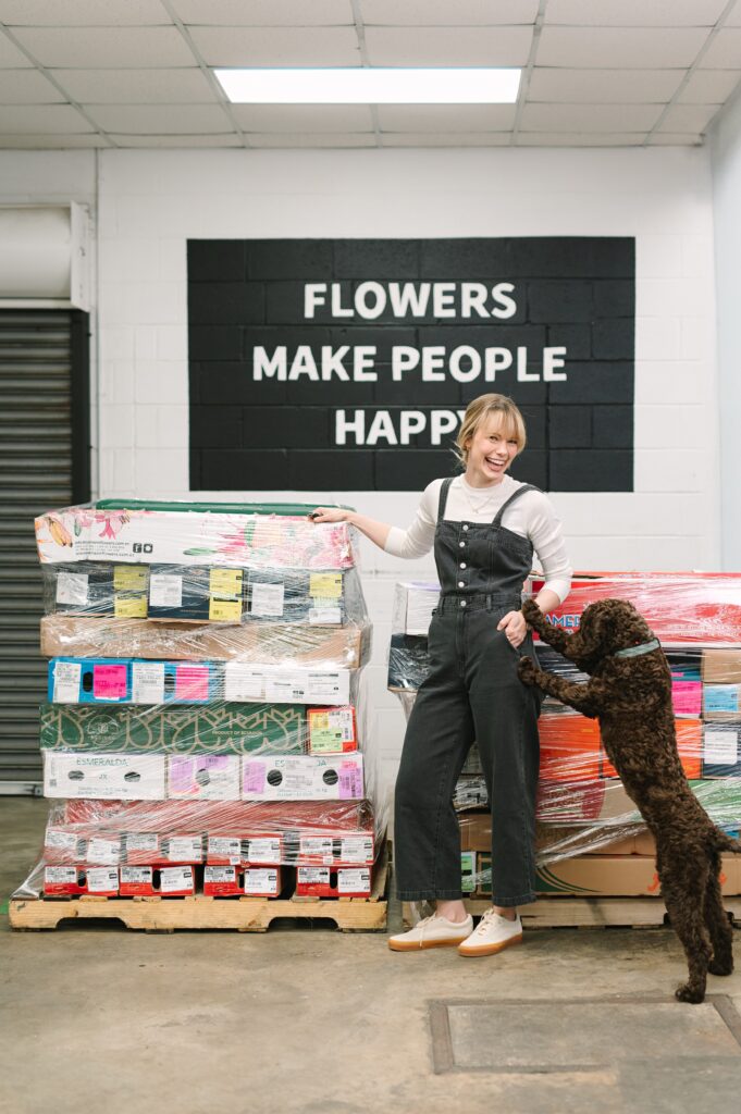 Candid branding photography of a flower market owner laughing with the shop dog inside the warehouse.
