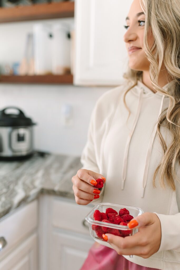 Fitness coach holding fresh raspberries in her kitchen during a lifestyle branding shoot