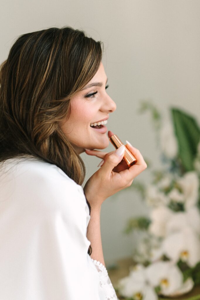 Bride smiles while putting on lipstick.