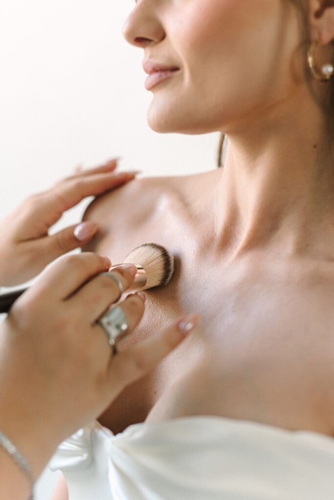 Detail photo of a makeup artist applying makeup to a bride's chest during a branding photography session.