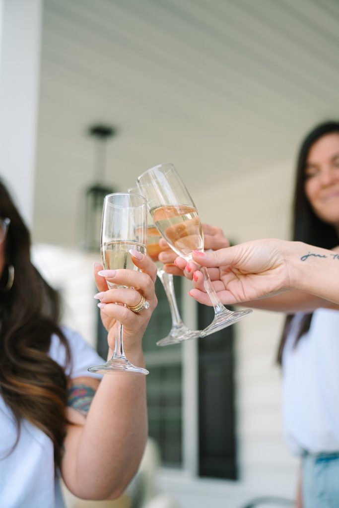 Close-up of hands clinking champagne glasses in a celebratory toast on a porch, Richmond VA branding photography