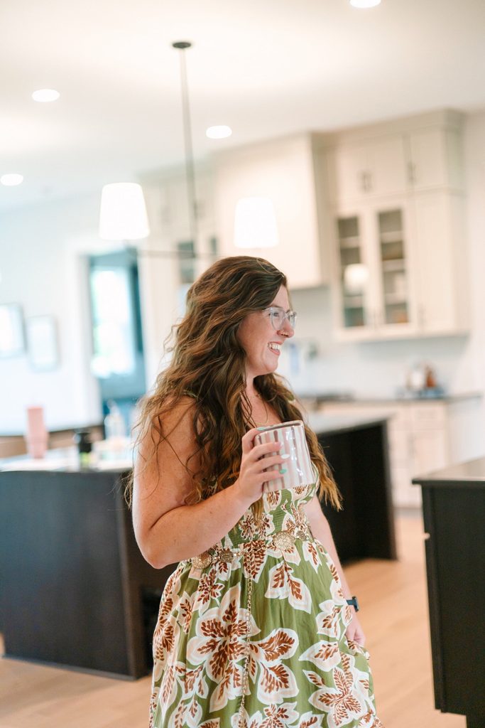 Laughing team member in a green floral dress holding a striped mug in a modern kitchen, candid Richmond VA branding photo