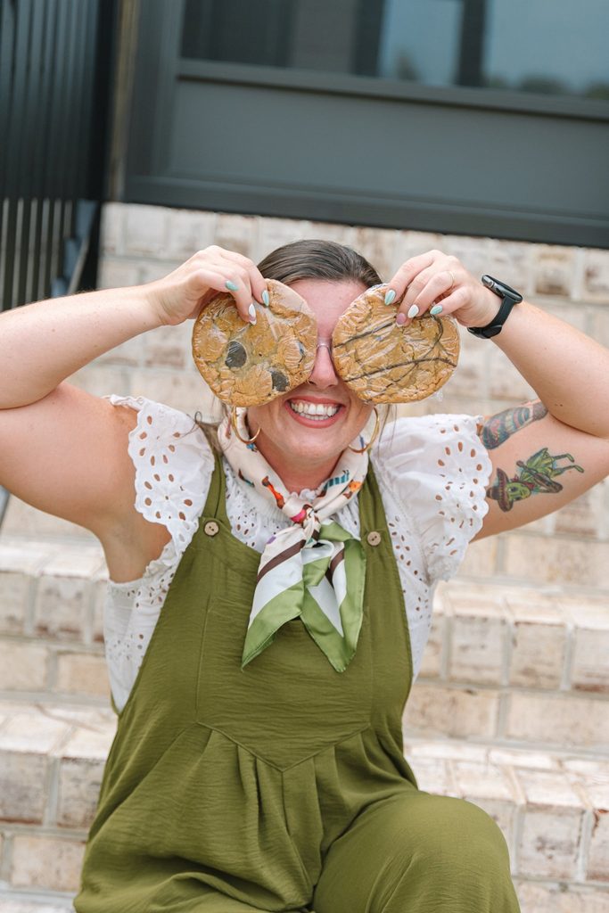 Playful Sparrow Home Loans team member holding two wrapped cookies over her eyes while sitting on brick steps