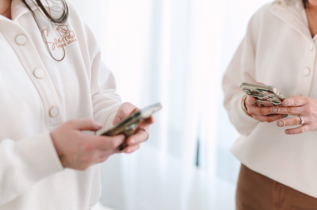 Two team members in cream Sparrow Home Loans embroidered sweatshirts using their phones, Richmond VA branding photography