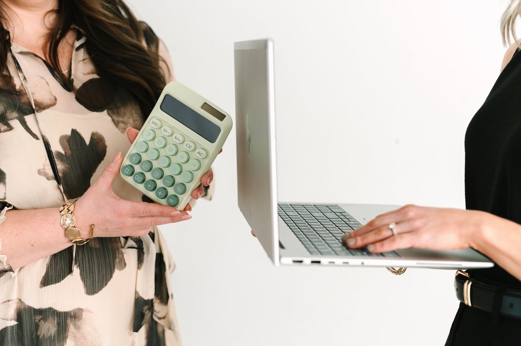 Close-up of one team member holding a sage green calculator beside another typing on a laptop, Sparrow Home Loans imagery