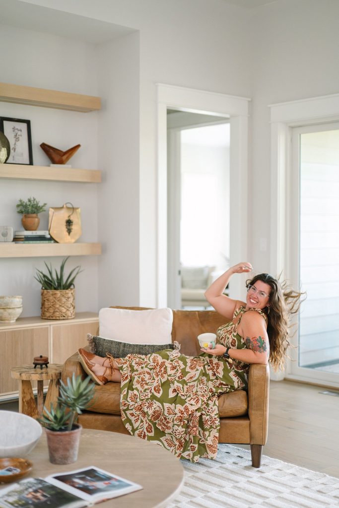 Team member lounging in a tan leather chair holding a teacup in a bright living room, Sparrow Home Loans brand imagery