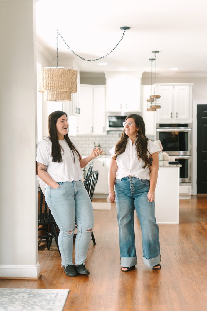Two team members in white tops and jeans chatting in a bright kitchen, Sparrow Home Loans brand imagery in Richmond VA