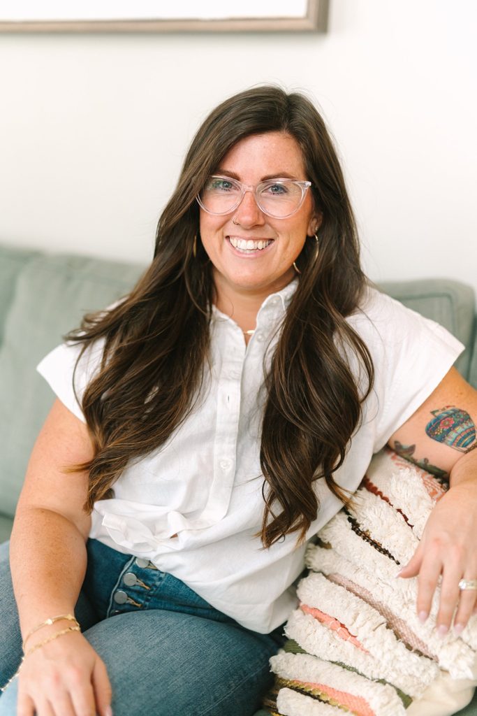 Smiling Sparrow Home Loans team member in a white button-up shirt sitting on a sage green sofa, Richmond VA branding headshot