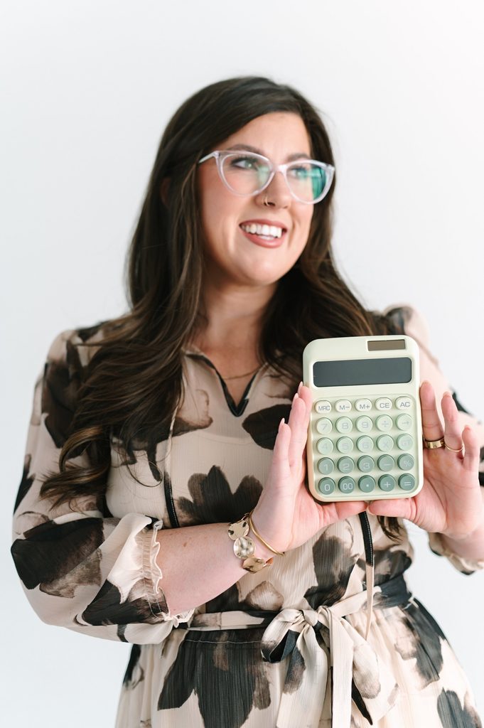 Smiling Sparrow Home Loans team member holding a sage green calculator against a white studio backdrop, Richmond VA