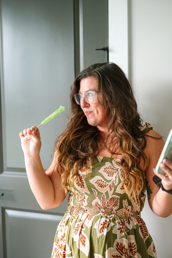 Team member in a green floral dress holding a green rock candy stick and her phone, playful Sparrow Home Loans social content