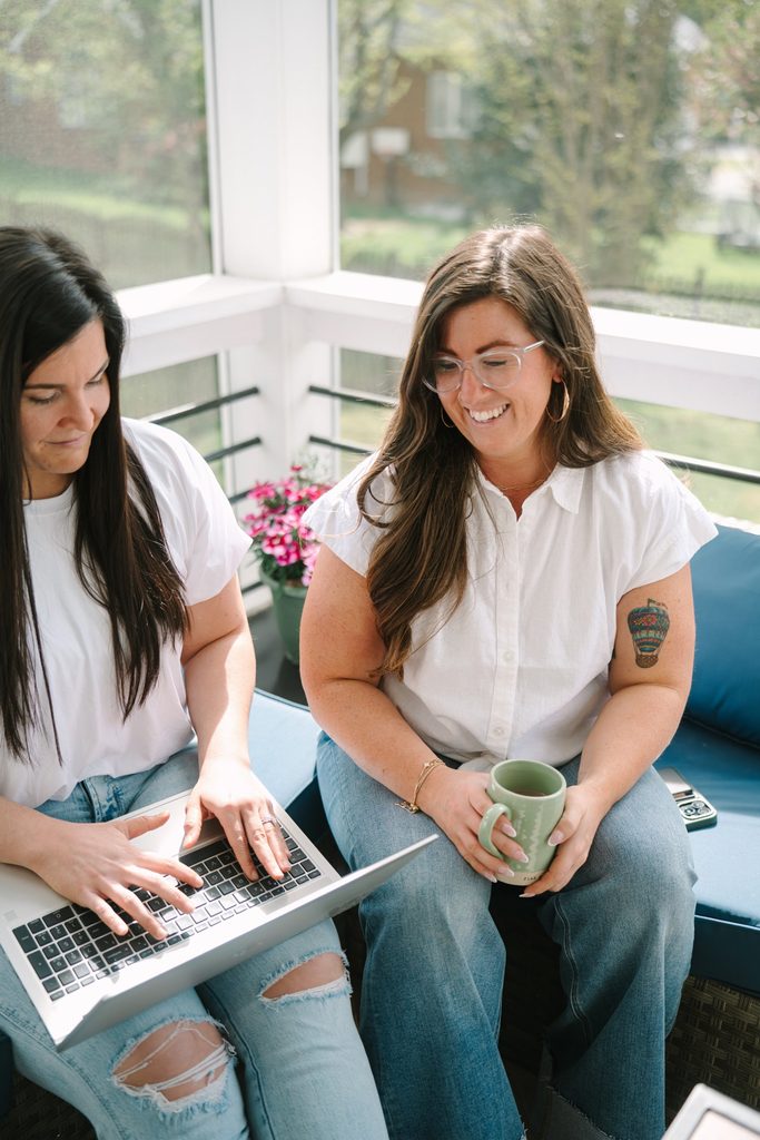 Two Sparrow Home Loans team members in white tops working together on a laptop on a sunny screened porch